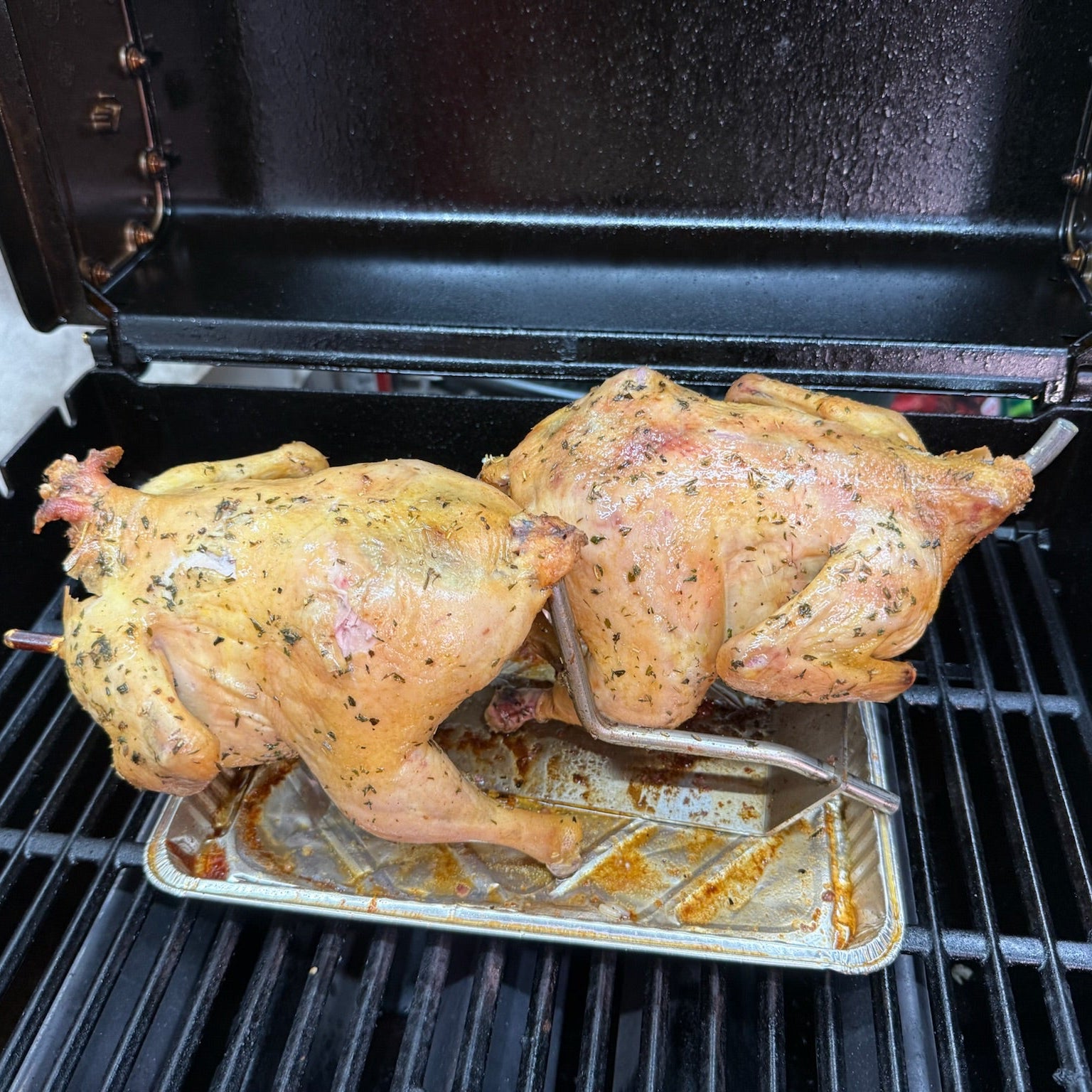 Two chickens on a grill with a metal tray underneath.